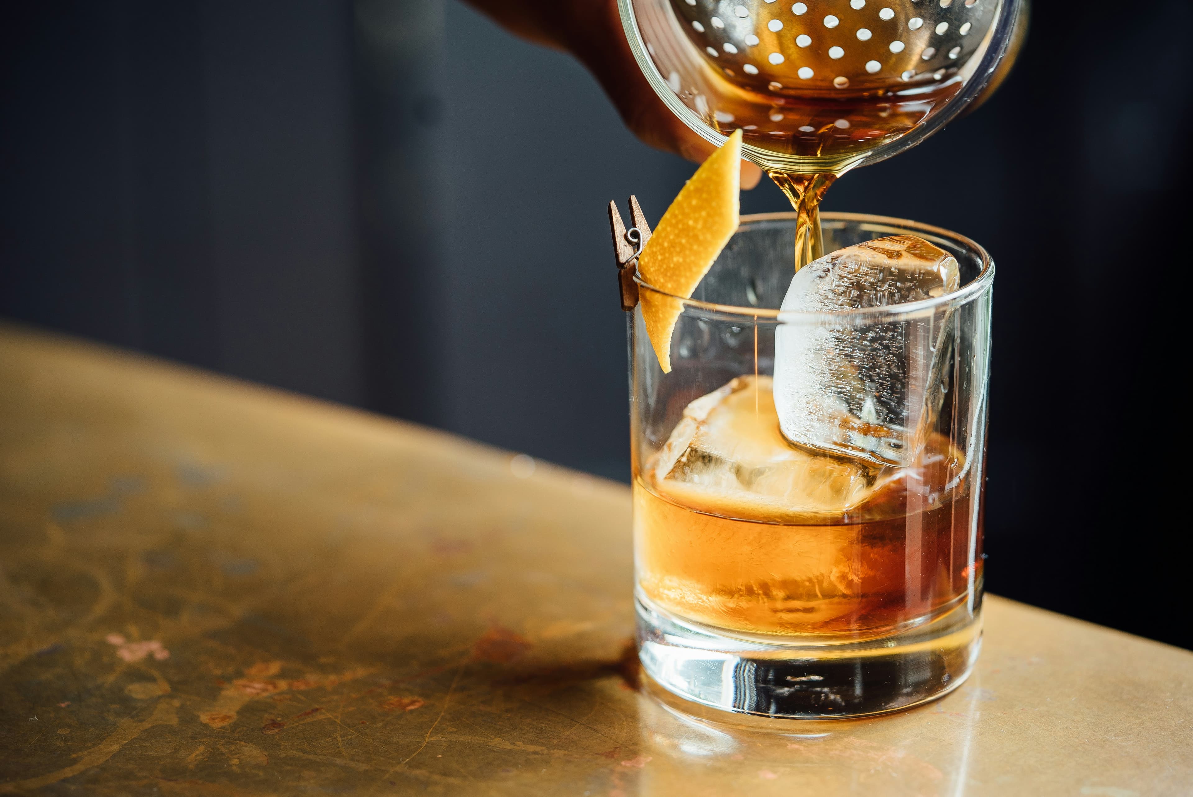 Bartender pouring a cocktail with an orange twist garnish
